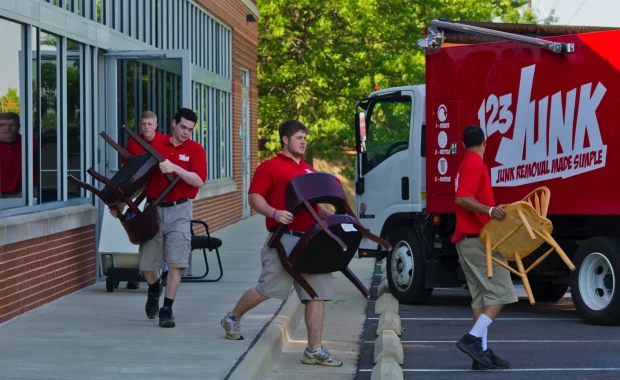 Three junk removal workers carrying chairs out of a building toward a red 123JUNK truck