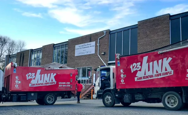 Two red 123JUNK trucks parked outside a brick community service building as workers walk toward the entrance