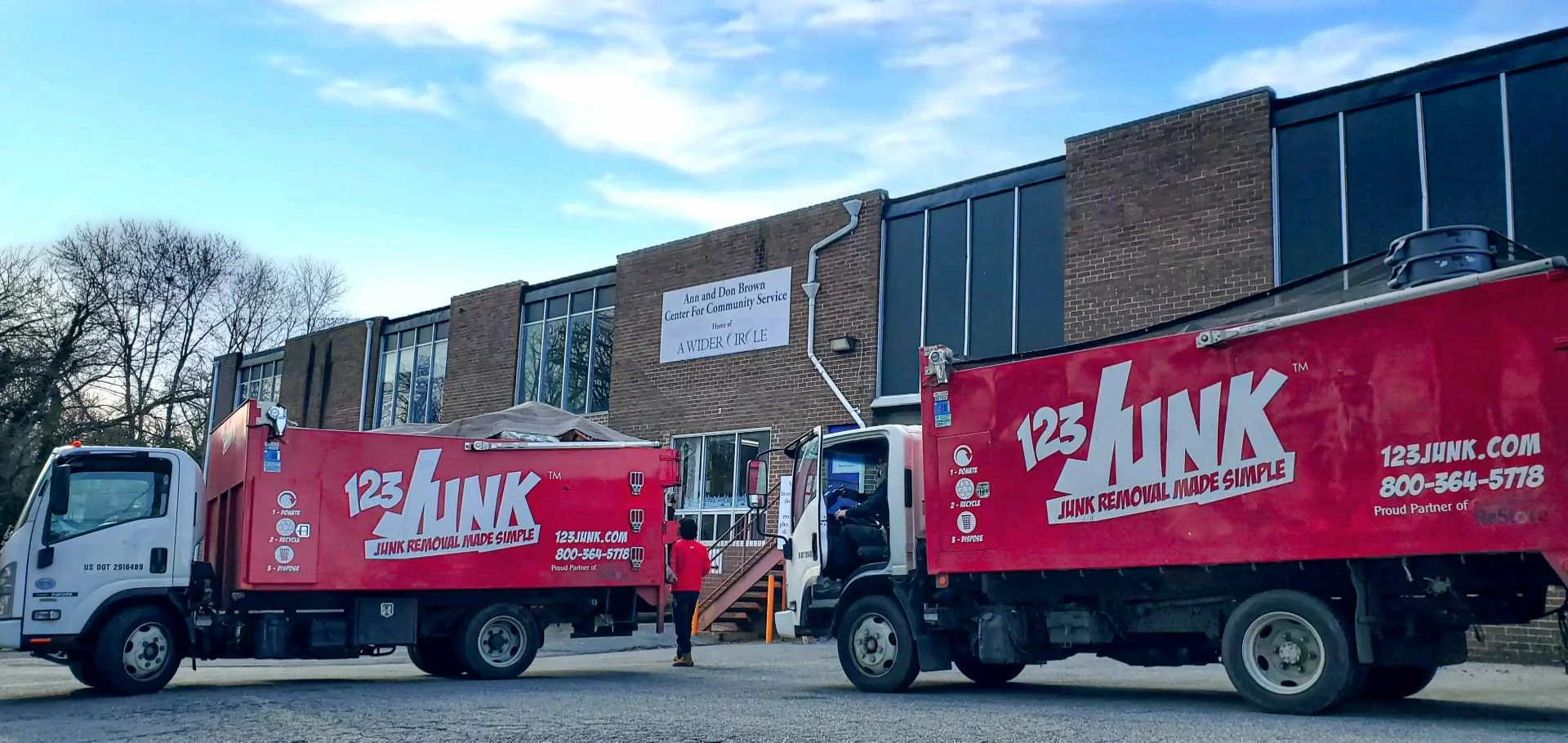 Two red 123JUNK trucks parked outside a brick community service building as workers walk toward the entrance