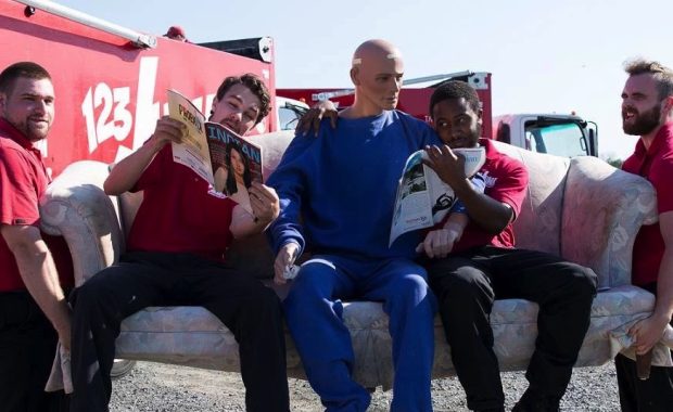 two men moving a couch with three men seated on it