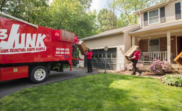 123JUNK team carrying furniture from a house to a red junk removal truck parked in the driveway