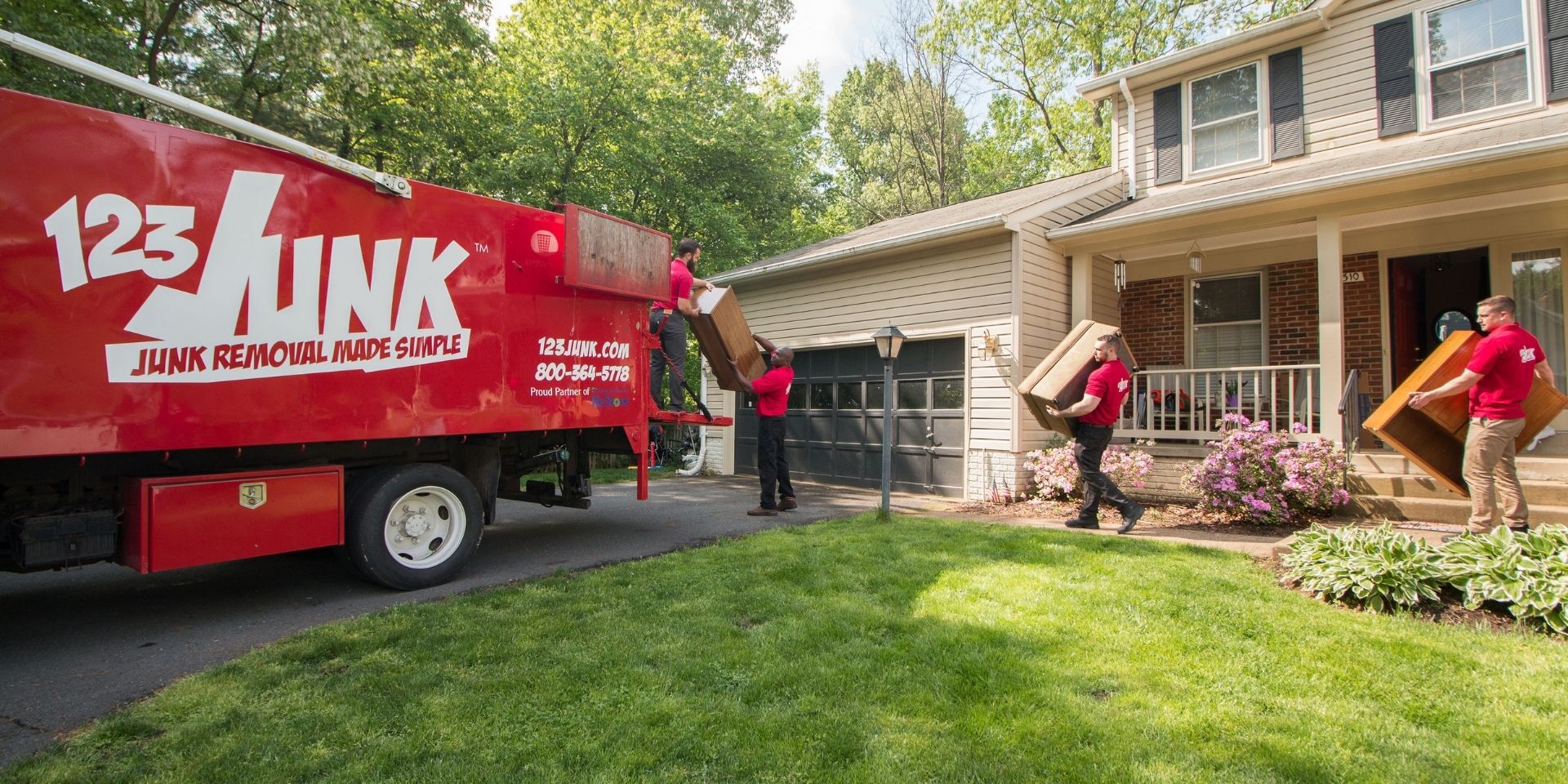 123JUNK team carrying furniture from a house to a red junk removal truck parked in the driveway