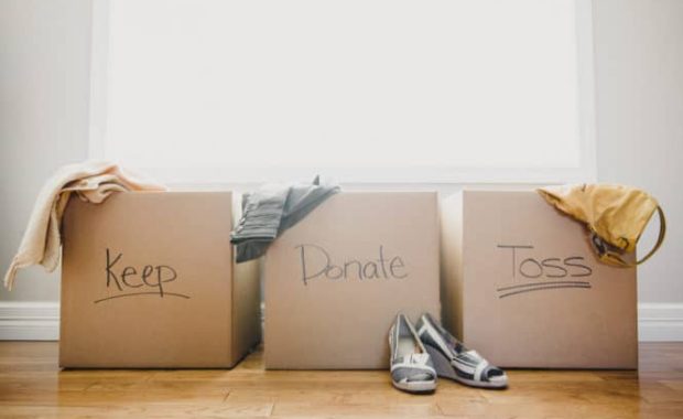 Three cardboard boxes labeled Keep, Donate, and Toss, with clothing and shoes placed around them
