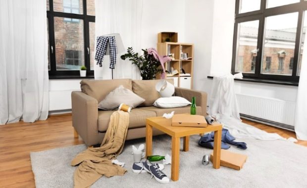 A messy living room with clothes, bottles, and other items scattered on the floor and furniture