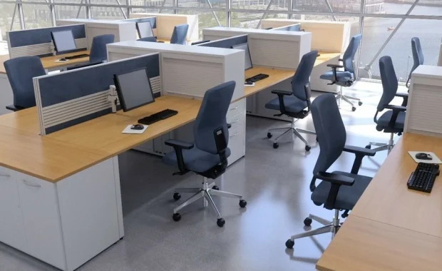 Modern open-plan office with rows of wooden desks, blue swivel chairs, and computer monitors, overlooking a river through large windows
