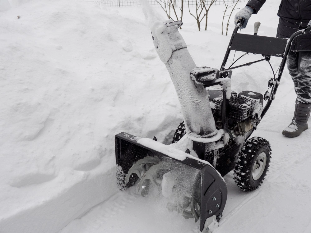 Person operating a snow blower to clear deep snow along a driveway