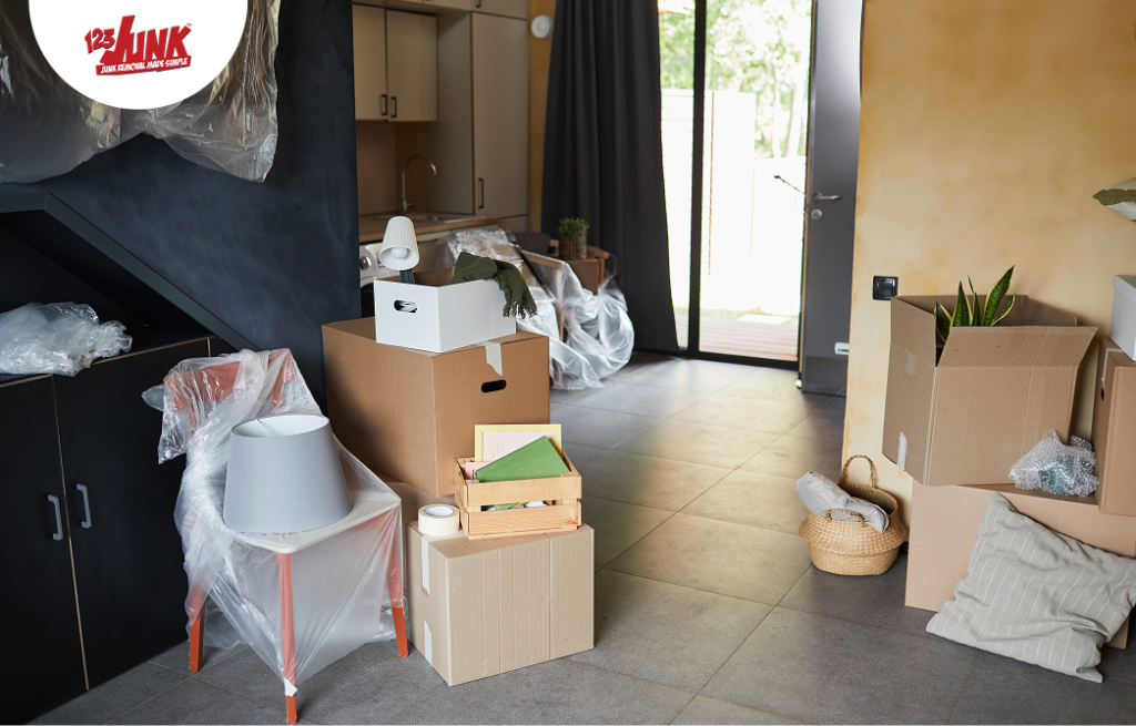 Interior of a home with various moving boxes, household items, and furniture partially packed and covered in plastic