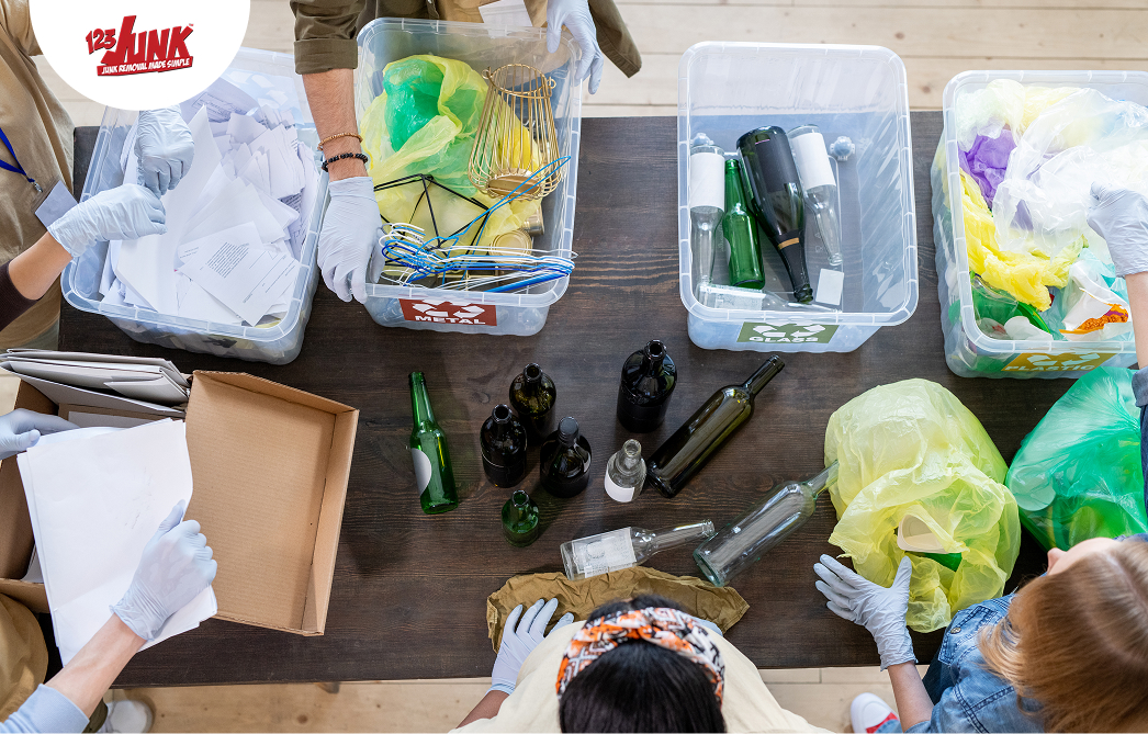 Overhead view of people wearing gloves sorting recyclables, including bottles, paper, and plastic bags, into labeled bins