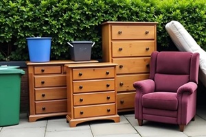 discarded household furniture and trash bins placed outside for collection on a sunny day