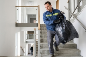 Junk Removal Worker Moving Heavy Trash Bag Down Through Modern Apartment Stairs